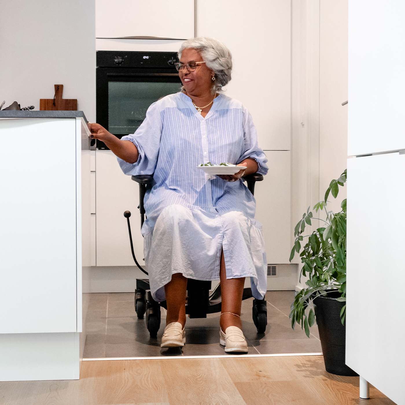 Elderly woman using a mobility chair as a walking aid while carrying a plate in her kitchen, illustrating how walking aids support safe mobility and independence at home.